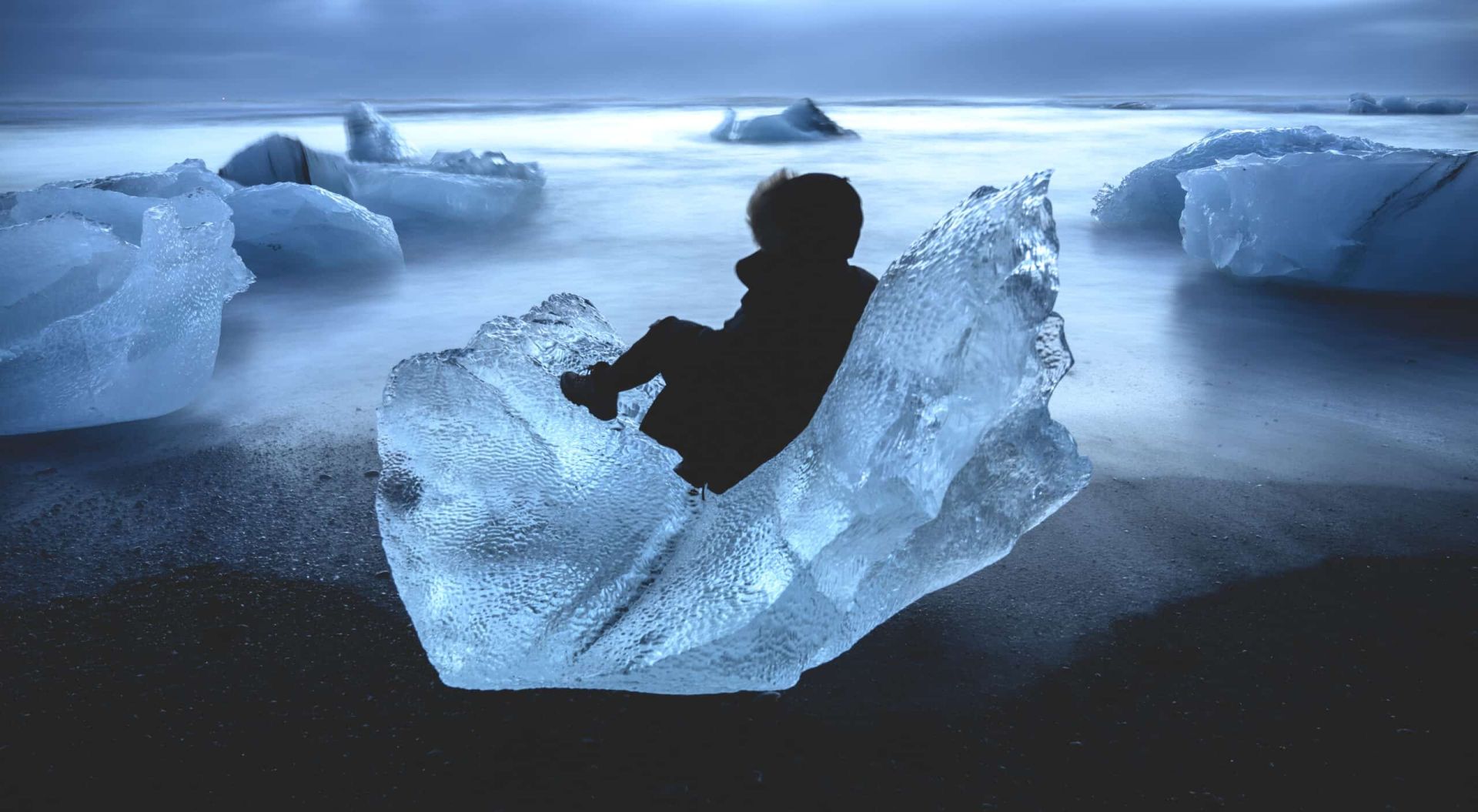 fotografía artística de una mujer vestida de negro sobre un gran hielo en la playa de los diamantes de islandia en un viaje organizado por all these humans