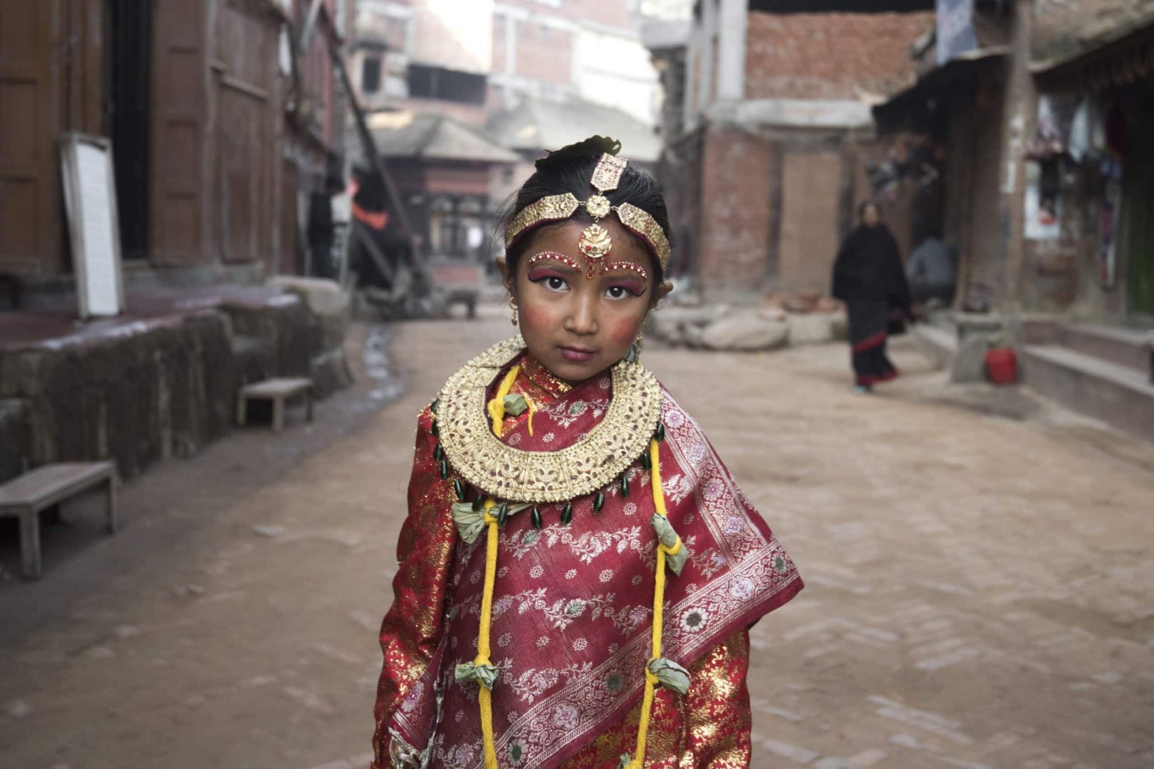 fotografía artística de retrato y viaje de una niña nepalí con vestido tradicional antiguo y con adornos dorados en medio de una calle de bhaktapur en nepal